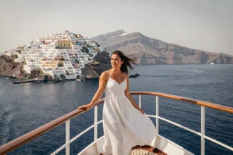 Femme sur le pont d'un bateau de croisière approchant la caldeira de Santorin avec vue sur les maisons blanches d'Oia