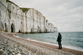 Falaises blanches de la Côte d'Albâtre en Normandie avec plage de galets et silhouette d'un randonneur au bord de la mer